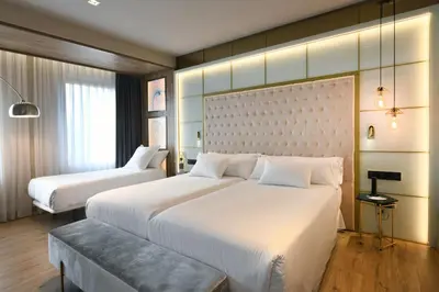 a hotel room with two beds and a bench at Barceló Ourense in Ourense