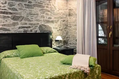 a bedroom with a bed with green pillows and a stone wall at Hotel Rua Villar in Santiago de Compostela