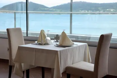 a table with a white tablecloth and chairs and a window at Apartamentos Las Sirenas in Viveiro