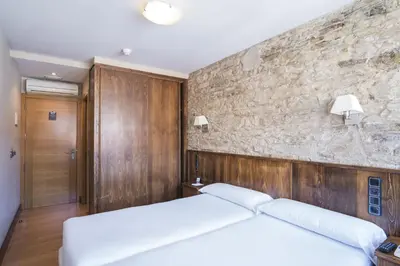 a bedroom with a white bed and a stone wall at Hotel Alda Avenida in Santiago de Compostela