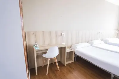 a room with two beds and a desk and a chair at Hotel Alda Avenida in Santiago de Compostela