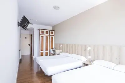 two beds in a room with a tv on the wall at Hotel Alda Avenida in Santiago de Compostela
