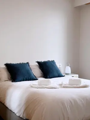 a large white bed with blue pillows on it at Estudio céntrico 2 con terraza y parking privado in Ourense