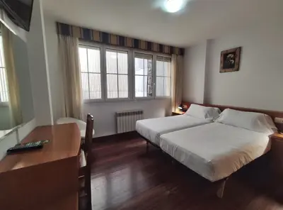 a bedroom with a bed and a desk and two windows at Hotel Hórreo by Bossh! Hotels in Santiago de Compostela