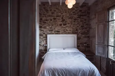 a bedroom with a white bed in a brick wall at Houmi As Bouzas in Castrelo de Miño