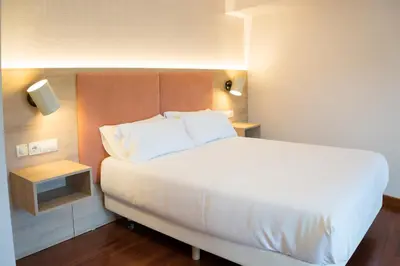 a bedroom with a large white bed and a night stand at Hotel Parking Miradoiro de Belvís in Santiago de Compostela