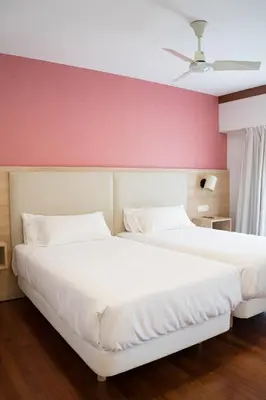 two beds in a bedroom with a pink wall at Hotel Parking Miradoiro de Belvís in Santiago de Compostela