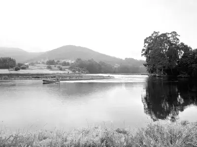a black and white photo of a river with a boat at The Cliffs - Passion Eccehomo in Viveiro