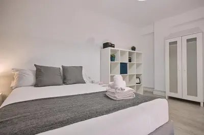 a white bedroom with a large bed with a white shelf at Dadá Coliving & Rooms by Serendipia Turismo in Santiago de Compostela