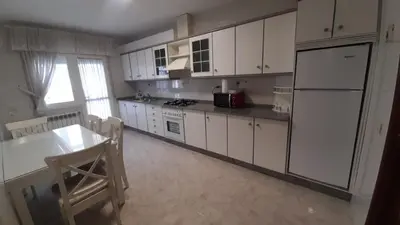 a kitchen with white cabinets and a table and a refrigerator at dpCristal Sarria Centro in Sarria