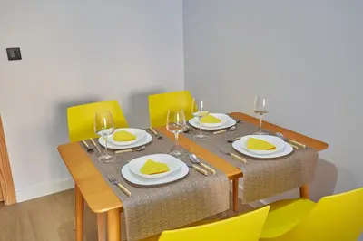 a dining room table with yellow chairs and a table with glasses at HAVANAAPARTAMENTOS in Puerto de Vega