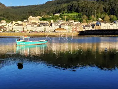 a boat in the water with a town in the background at La Casa de Ana in Viveiro