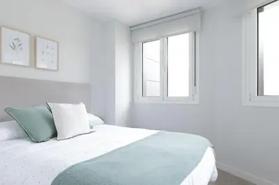 a white bedroom with a bed with two windows at Apartamentos Nature in Cangas del Narcea