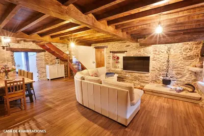 a living room with white furniture and a stone wall at Viveiro Río Pedroso in Vivero