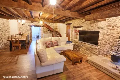 a living room with white furniture and a stone wall at Viveiro Río Pedroso in Vivero