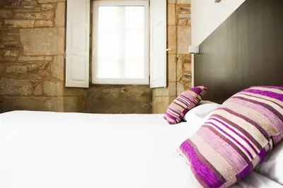 a white bed with purple pillows and a window at Hotel A Tafona do Peregrino in Santiago de Compostela