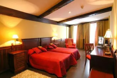 a bedroom with two beds with red sheets and a desk at Hostal Santo Grial in Santiago de Compostela
