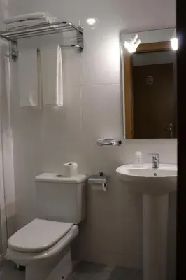 a white bathroom with a toilet and a sink at PENSIÓN RÚA in Arzúa