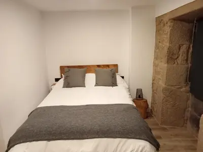 a bedroom with a white bed with a stone wall at A Casiña da Ponte in Padrón