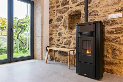 a wood stove in a room with a stone wall at A casa de Abaixo, aloxamento rural in Vedra