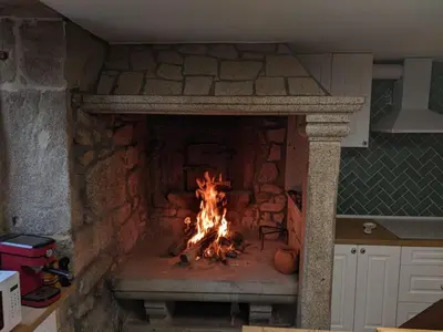 a fire in a stone fireplace in a kitchen at El cobijo de Soar ¡Casa rural completa! in Moraña