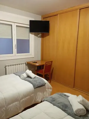 a bedroom with two beds and a desk and a table at Pensión Abeledo in Sarria