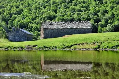 an old building on a hill next to a body of water at VUT El Refugio in Villablino