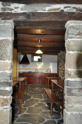 a kitchen with wooden tables and a stone wall at A Horta de Abel in Tríacastela