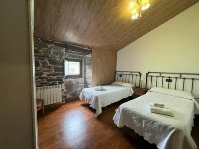 a room with two beds and a stone wall at A Horta de Abel in Tríacastela