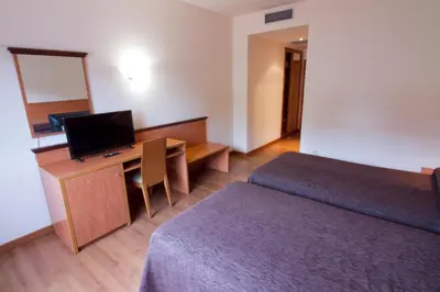 a room with two beds and a desk with a television at Hotel Torques in A Coruña
