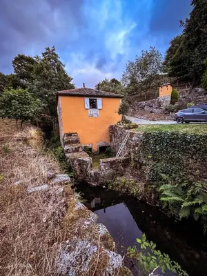 an orange house on a stone wall next to a pond at EL VIEJO MOLINO in Lugo
