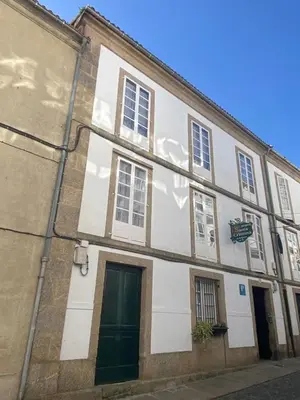 a white building with a green door on a street at Casa Anglicana del Peregrino/ Pensión Santa Cristina in Santiago de Compostela