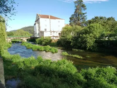 a river with a bridge and a building in the background at O balcón do Río in Caldas de Reis